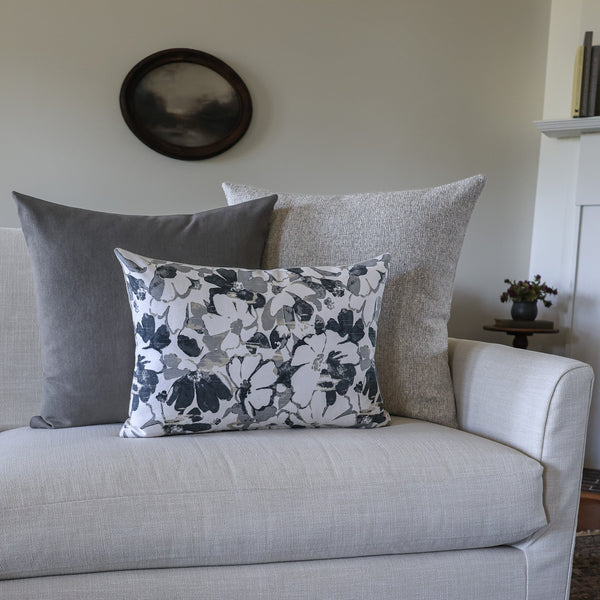 Gray and black designer pillow covers styled on a cream sofa, featuring a floral lumbar pillow layered with solid charcoal gray and textured neutral decorative throw pillows by HACKNER HOME.