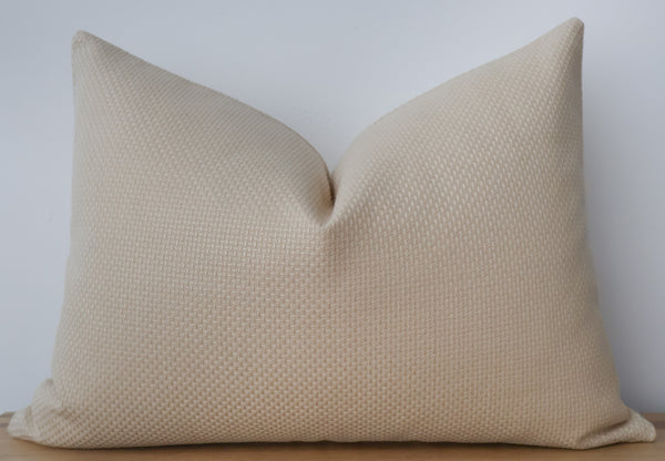 A square beige throw pillow with a textured, waffle-like fabric surface, shown against a neutral light gray background.