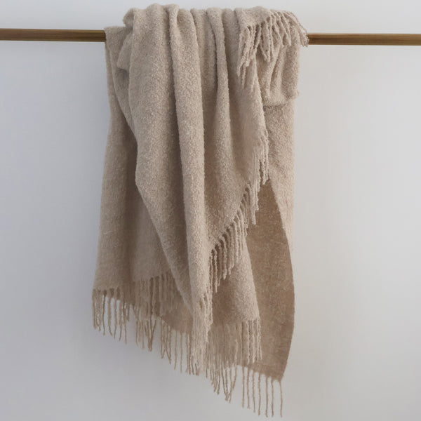 Beige Alpaca Wool blanket with fringes draped over a wooden rod against a white background