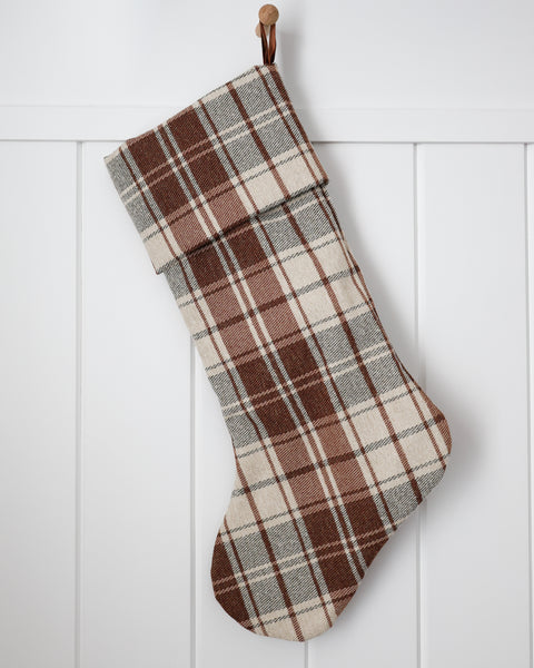 Red-brown plaid Heritage Christmas stocking displayed with evergreen garland and traditional holiday decorations