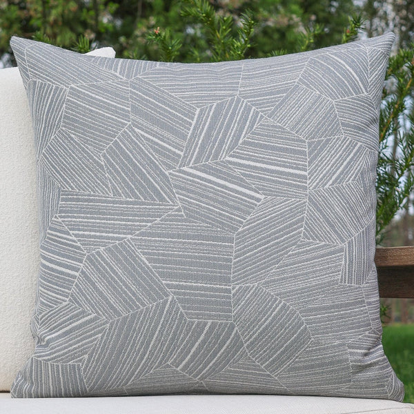 Gray geometric patterned pillow on a white surface with greenery in the background
