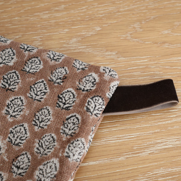 Close-up of a handmade Christmas stocking in a brown and white block-printed leaf pattern with a soft velvet hanging loop on a wooden surface.
