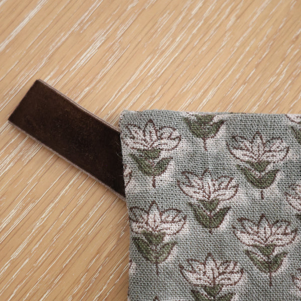 Close-up of muted blue floral block print Christmas stocking showing detailed linen texture and dark brown velvet hanging loop on a wood surface.