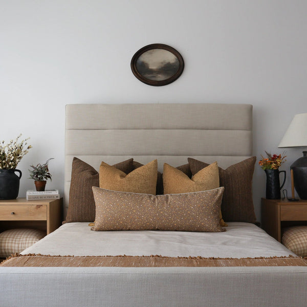 Bedroom styled with Hackner Home Patina Café velvet pillow covers in warm brown tones, layered on a neutral upholstered bed with beige and gold accent pillows for a cozy modern look.